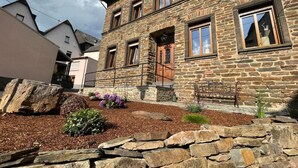 Ein Gebäude aus Stein mit zahlreichen Fenstern, einer Steinsitzbank und einem Garten mit Mulch und Pflanzen.