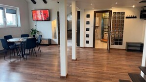 A spacious room with a wooden floor, a dining area with chairs, a television mounted on the wall, and a staircase leading to an upper level. - Carpatia Loft (Unknown)