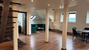 A spacious loft-style room with a wooden floor, a dining area with a table and chairs, a green sofa, and a staircase. - Carpatia Loft (Unknown)