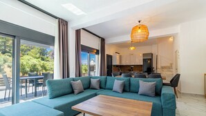 Ein modernes Wohnzimmer mit einer Eckcouch, einem Holztisch und einem großen Fenster mit Blick ins Freie.