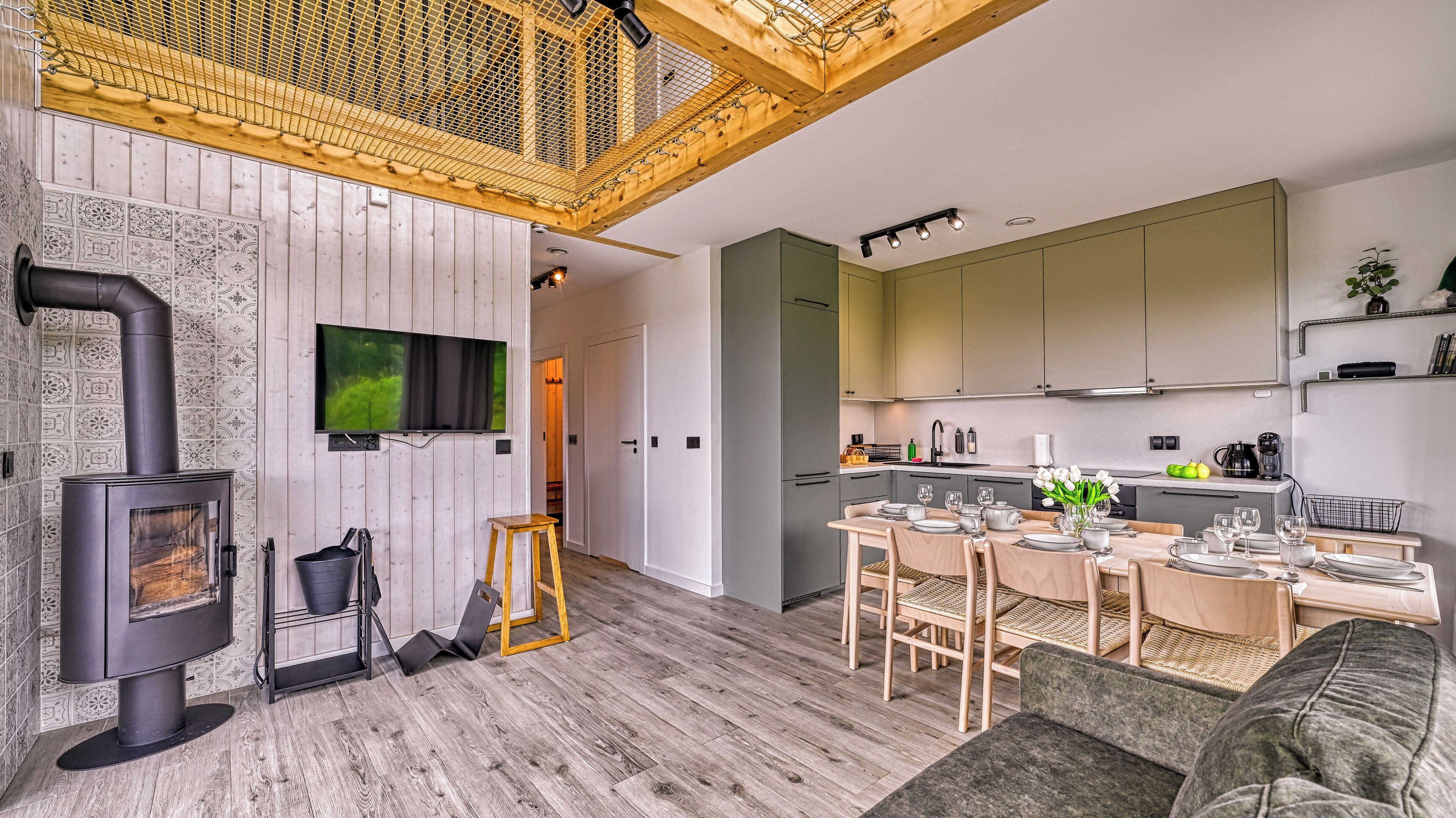 A modern kitchen with a dining area, a large flat-screen TV, and a wood-burning stove.