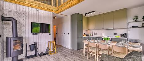 A modern kitchen with a dining area, a large flat-screen TV, and a wood-burning stove.