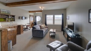 A spacious living area with a sofa, a coffee table, a TV, and a kitchen area with wooden cabinets and a bar. - Seaside Suites (Woody Point)