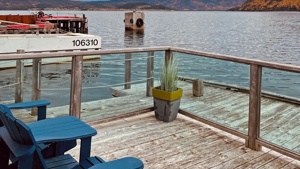 A wooden deck with a railing, a potted plant, and blue chairs. - Seaside Suites (Woody Point)