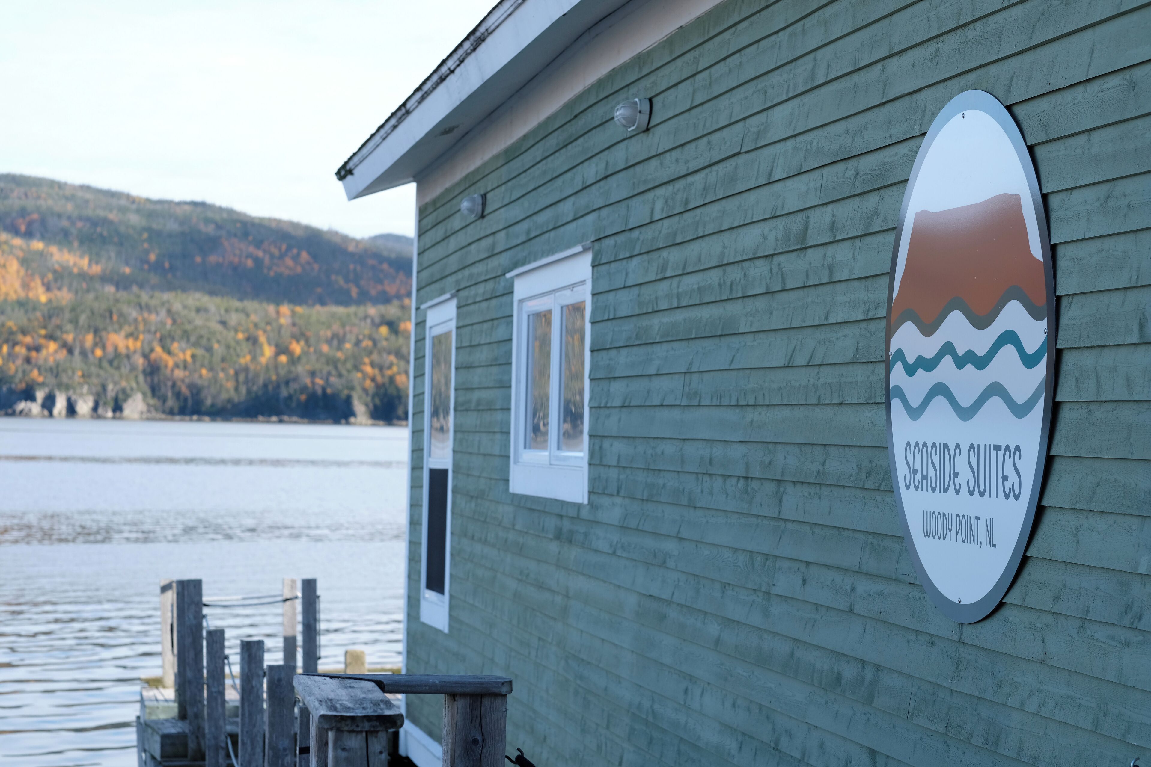 A wooden building with a sign reading "Seaside Suites, Woody Point, NL".