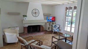 A living room with a fireplace, a television, wicker chairs, and a view through a window. - Typical Landes villa Seignosse le Penon (Seignosse)