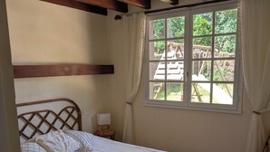 A bedroom with a bed, wooden beams, a window with curtains, and a view of an outdoor play area. - Typical Landes villa Seignosse le Penon (Seignosse)