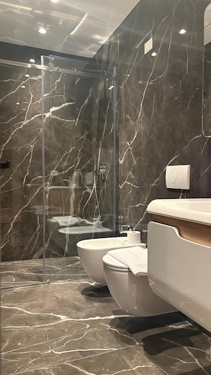 A modern bathroom with a glass-enclosed shower, two toilets, and marble flooring.