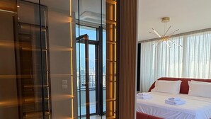 Une chambre d’hôtel moderne dotée d’un grand placard avec porte coulissante, d’un lit avec une literie rouge et d’une vue sur la ville grâce à de grandes fenêtres du sol au plafond.
