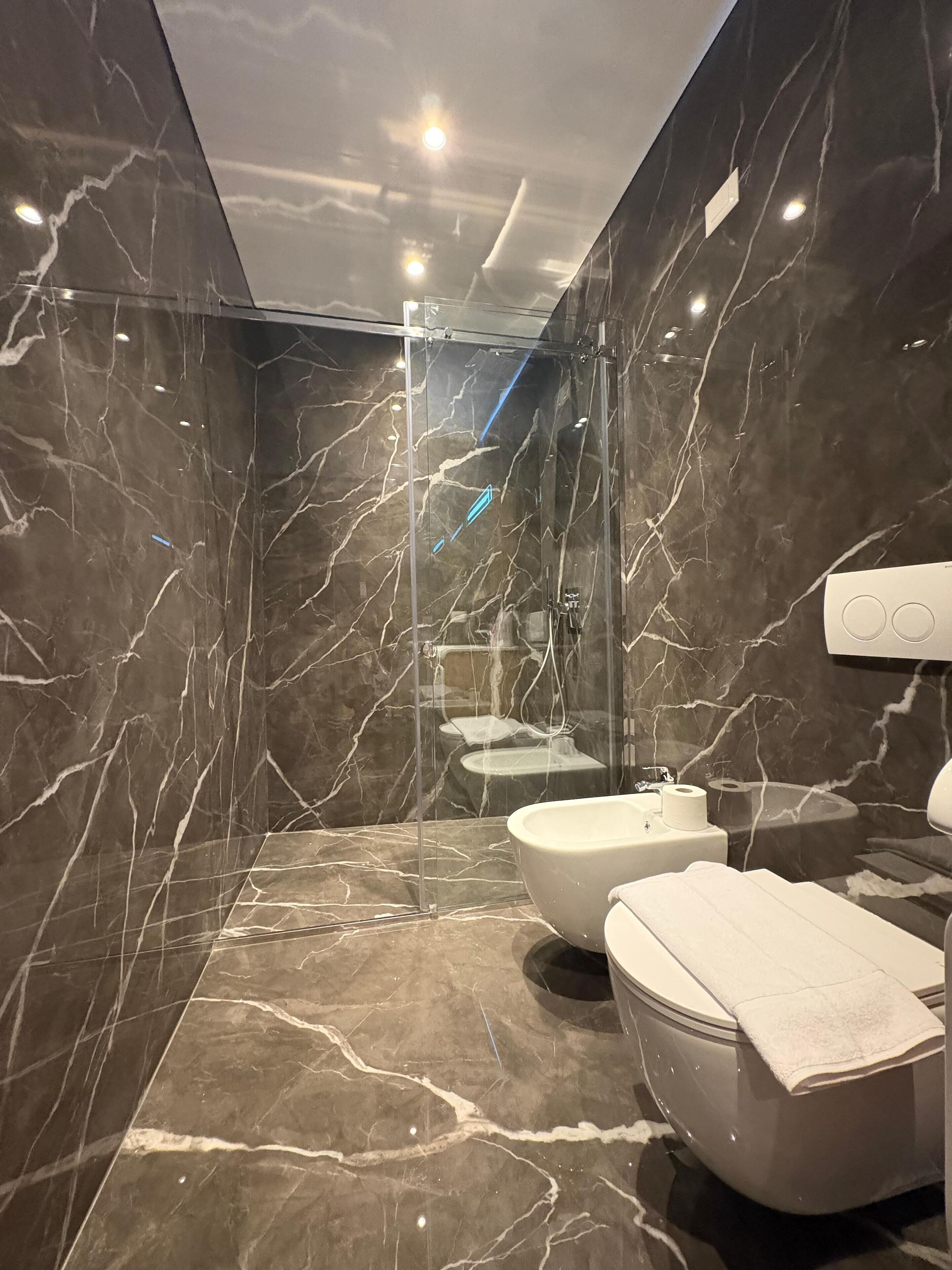 A modern bathroom with marble walls, a glass-enclosed shower, and two sinks.