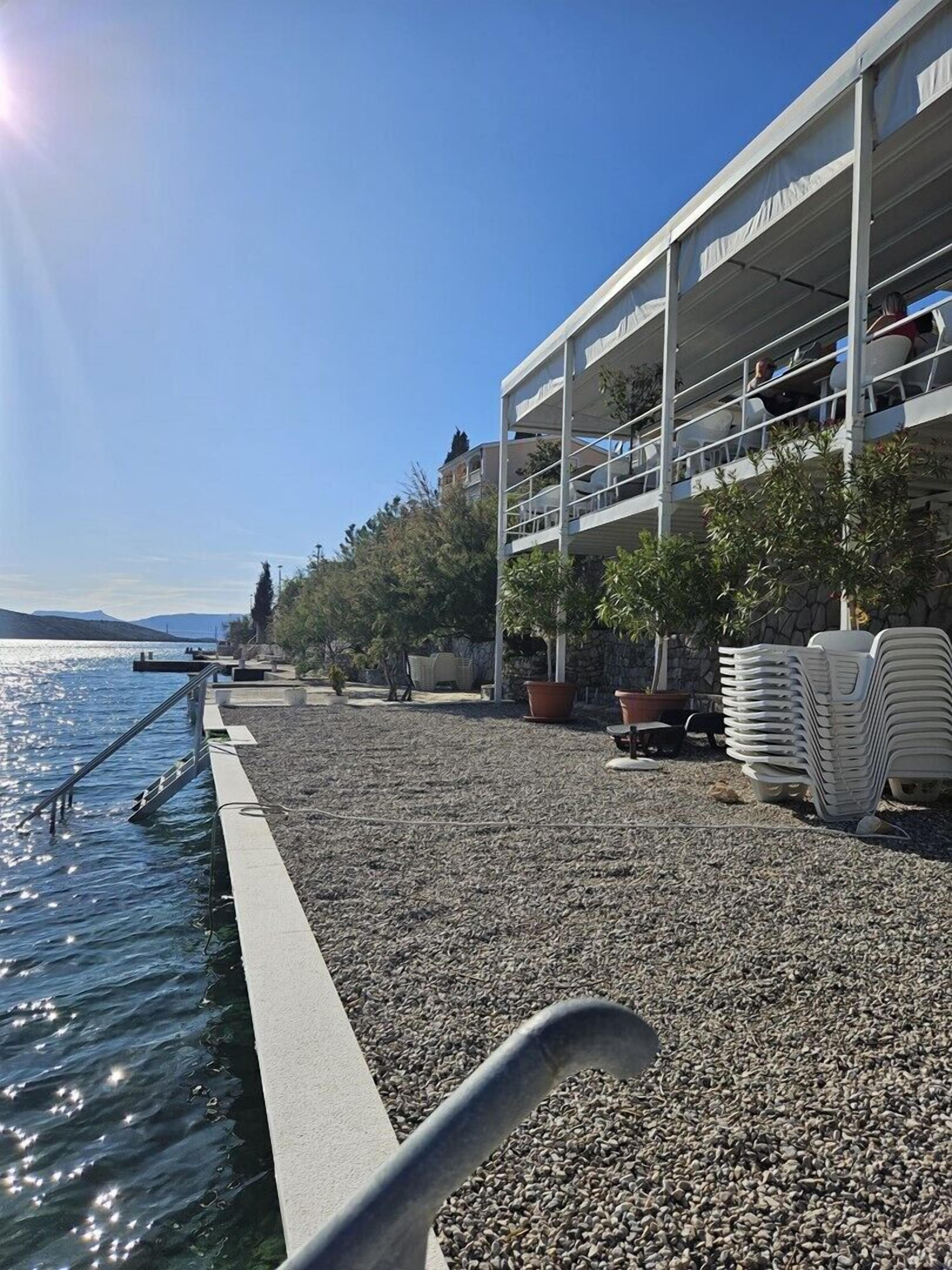 Ein Gebäude am Wasser mit Balkonen, die auf das Meer blicken, einem Kiesstrand und Topfpflanzen.