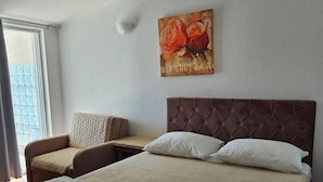 Une chambre d’hôtel avec un grand lit, un canapé, un tableau représentant des roses et une fenêtre donnant sur un beau paysage.