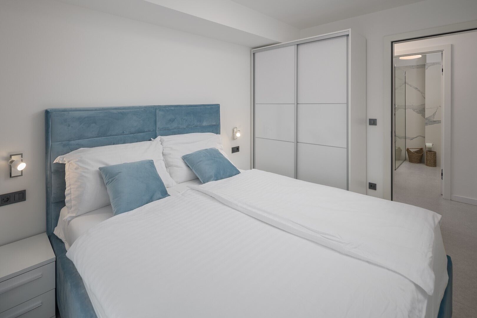 A modern bedroom with a large bed, a blue headboard, and a walk-in closet.