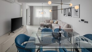 A modern living room with a glass dining table, blue chairs, a sofa, and a TV. - Apartman Blue in Poreč (Poreč)