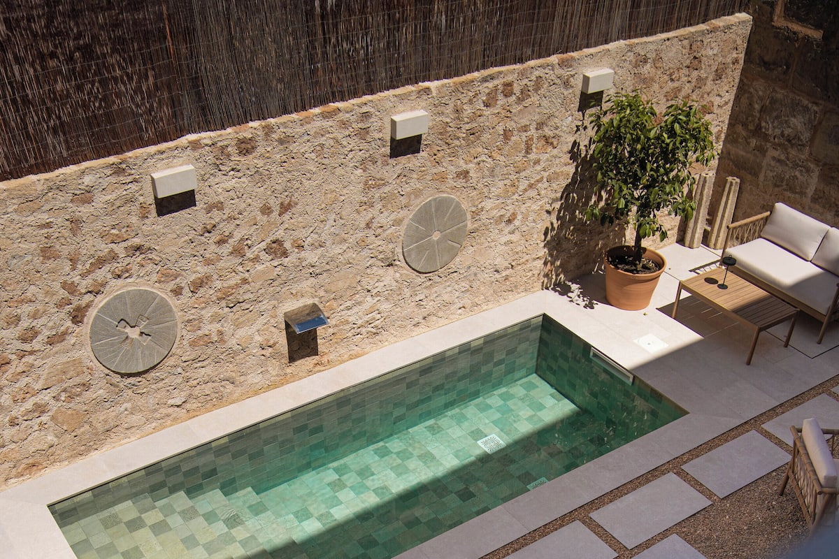 Une piscine extérieure avec des murs en pierre, une plante en pot et un espace détente avec une chaise et une table.