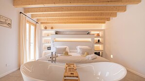 Un baño moderno con una bañera grande, vigas de madera en el techo y un mueble de tocador con estantes.