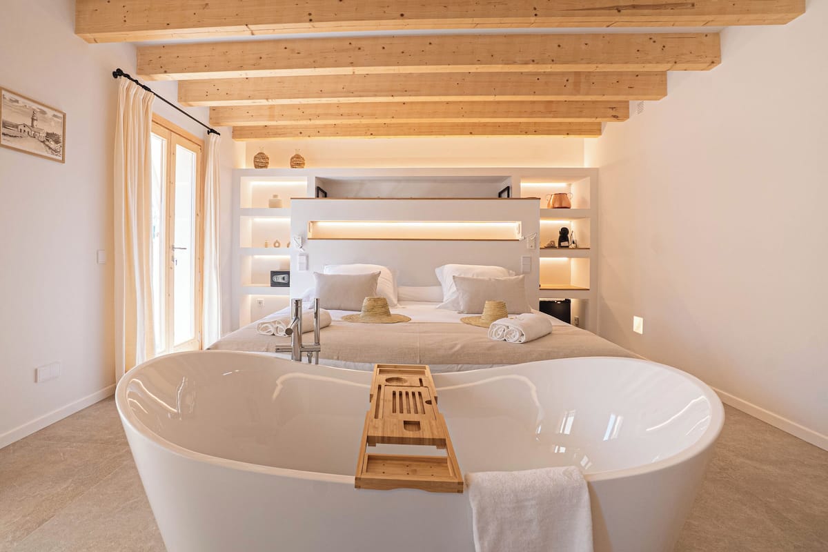 Une salle de bain moderne avec une grande baignoire, des poutres apparentes en bois au plafond et un meuble-lavabo doté d’étagères.
