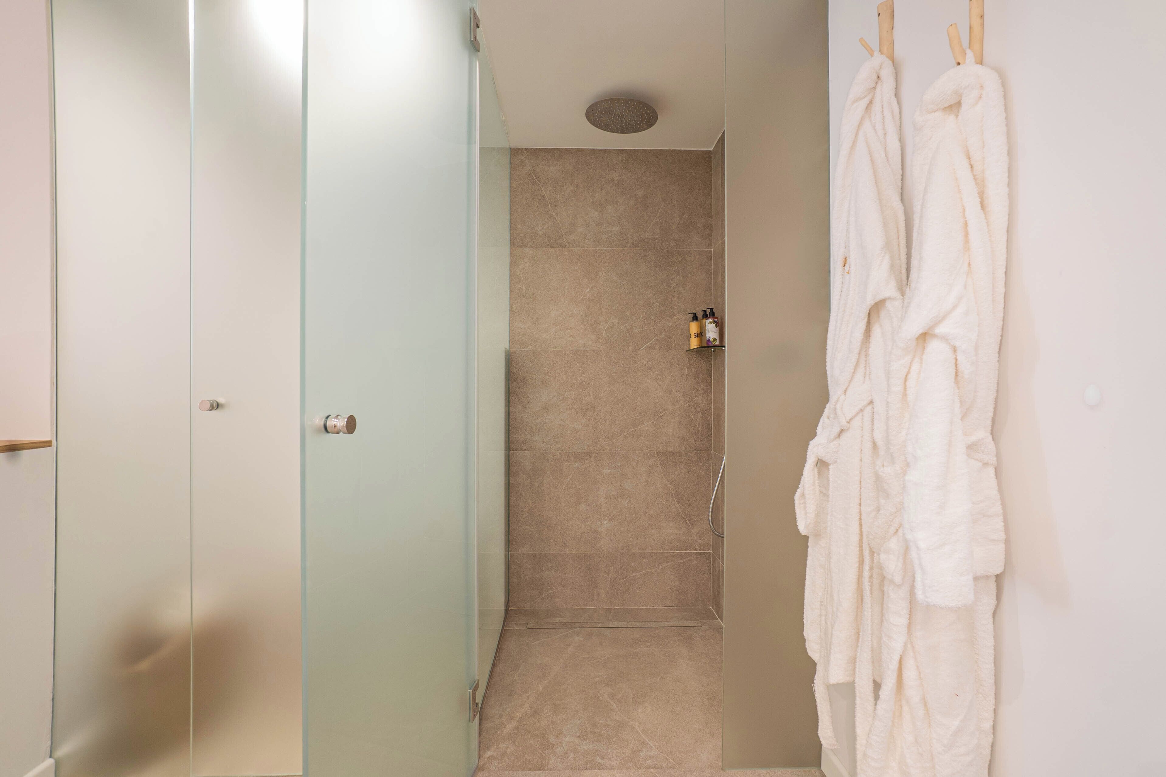 A bathroom with a glass shower enclosure, a towel rack with towels, and a small shelf with toiletries.