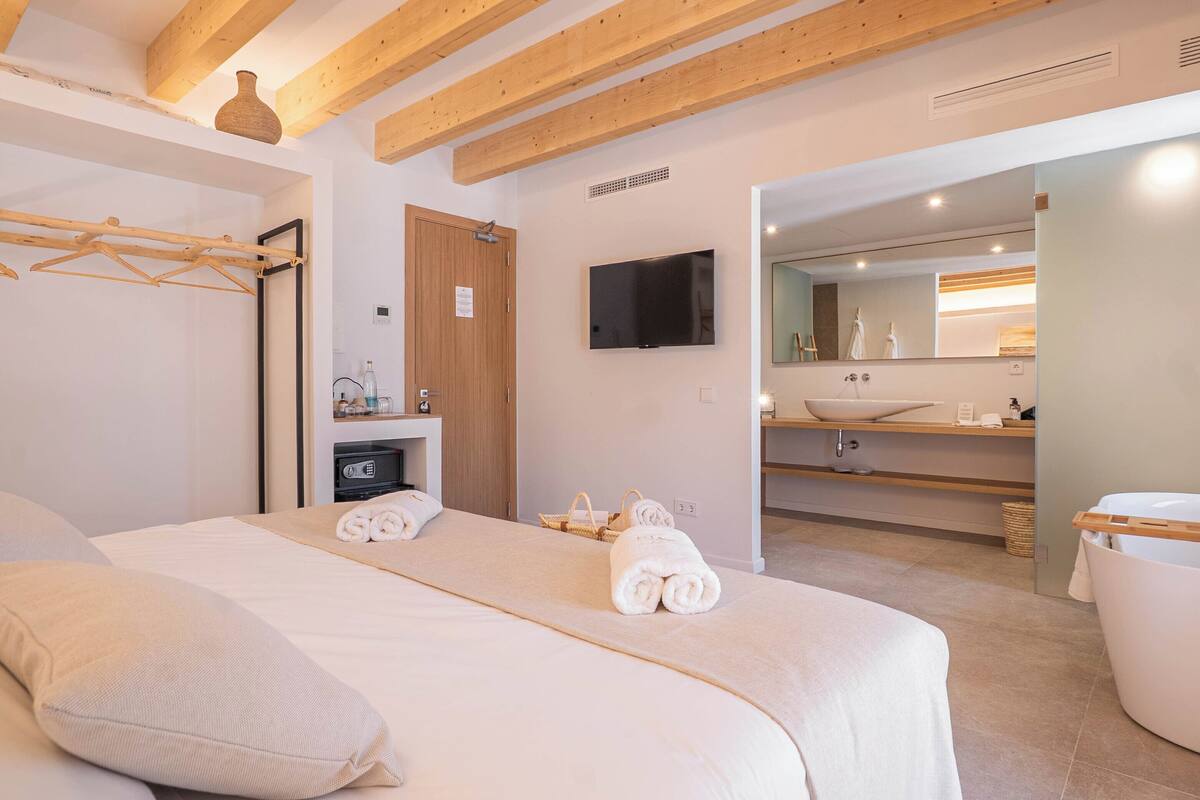 Une chambre d’hôtel avec un lit, une télévision, un plafond en bois, une salle de bain avec un lavabo et un miroir, et des serviettes sur le lit.