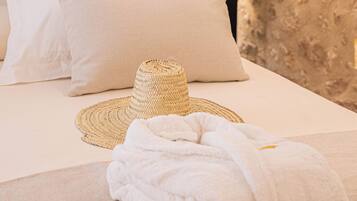 A neatly made bed with white linens, a woven hat, and a rolled towel.