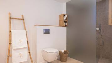 Un baño con inodoro, estante de madera con artículos de aseo, cesto de mimbre y zona de ducha.