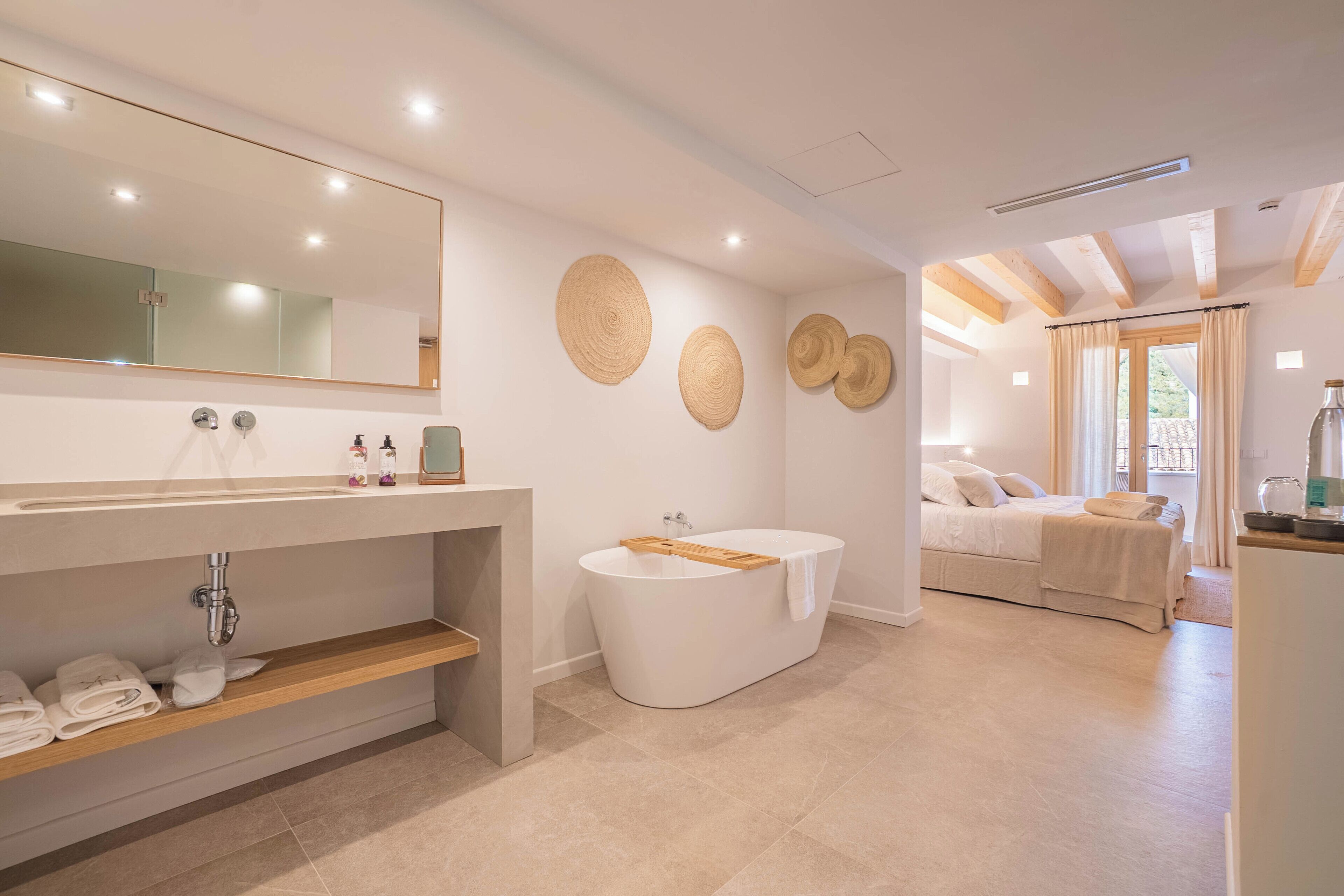 Een moderne badkamer met een vrijstaand bad, een grote spiegel en een houten plank met handdoeken.