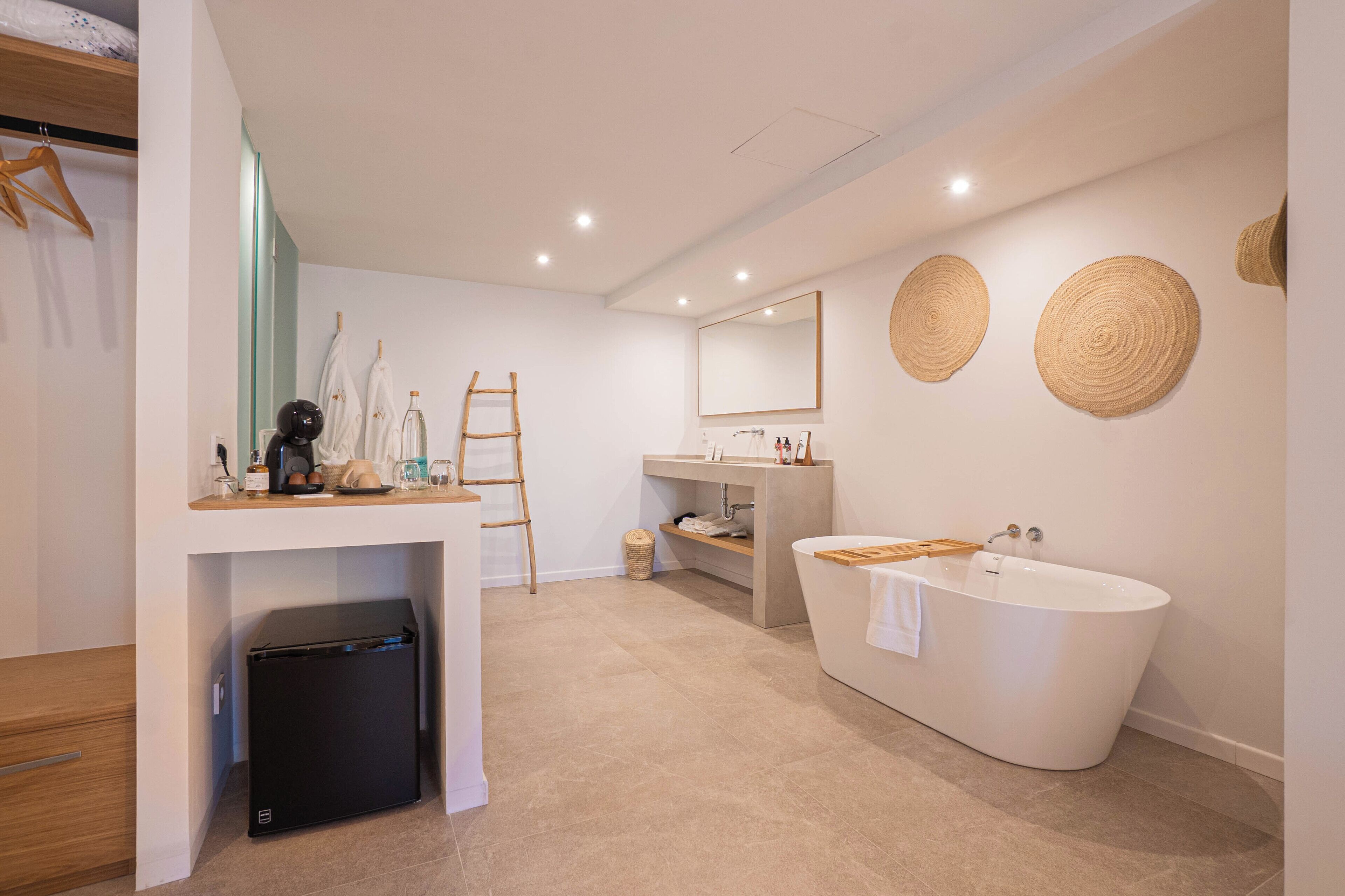 Un baño moderno con una bañera independiente, un tocador con espejo y un pequeño refrigerador debajo de la encimera.