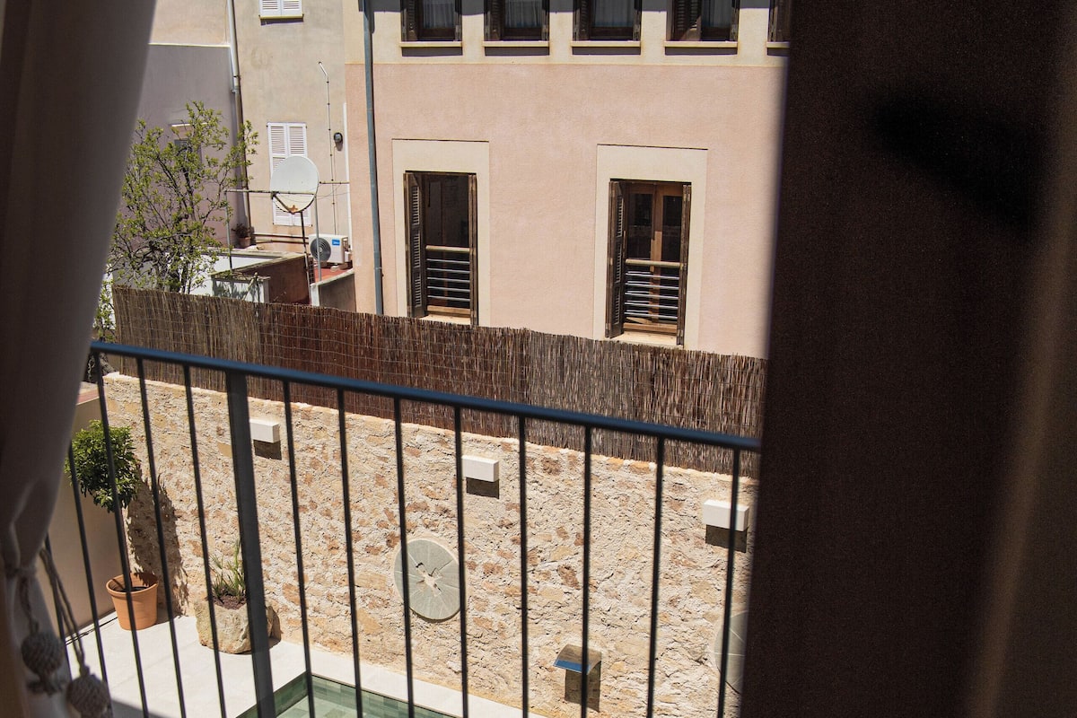 Un balcon donnant sur une cour, une piscine et un bâtiment avec un toit en tuiles.
