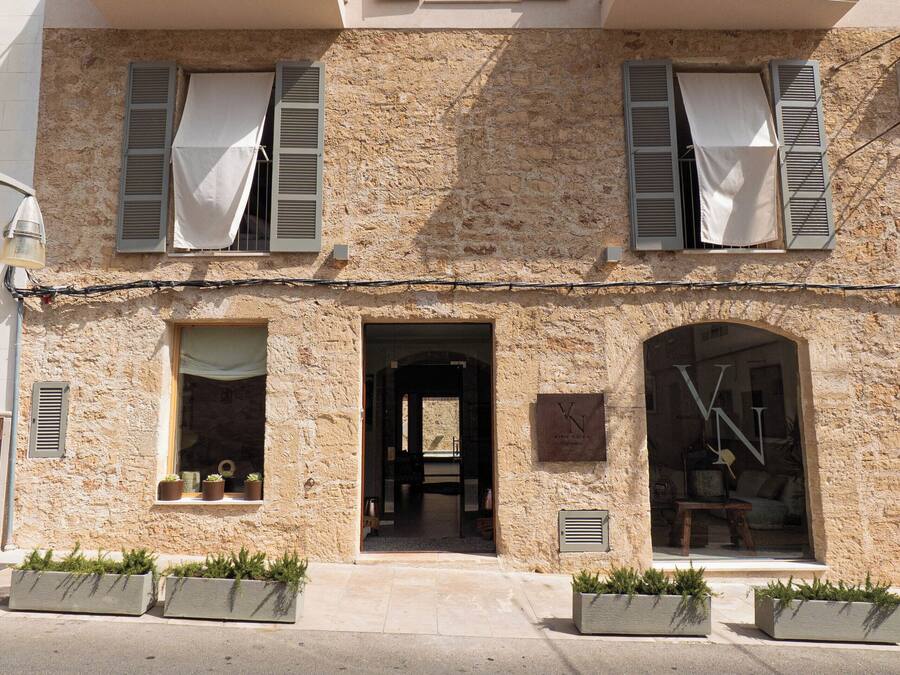 Un edificio de dos pisos con balcones, entrada a nivel de calle y plantas en macetas.