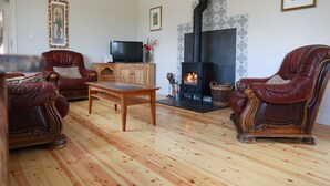 Een woonkamer met twee leren fauteuils, een houten salontafel, een televisie en een open haard.