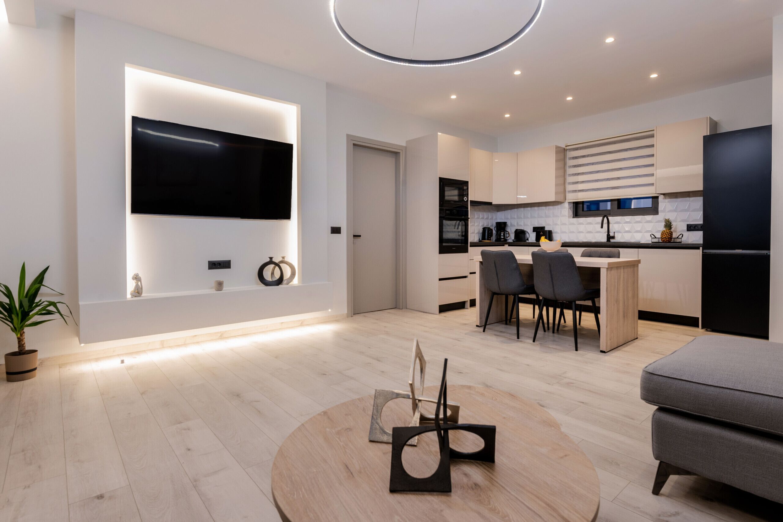 Una cocina moderna con un televisor de pantalla plana, una zona de comedor con una mesa redonda y un sofá gris.