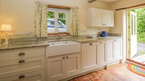 A kitchen with a sink, cabinets, and a window with curtains. - Keepers Cottage (Devizes)