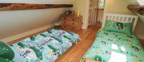 A bedroom with two beds, wooden flooring, a dresser, a window, and a door leading to another room.