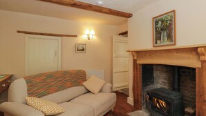 A cozy living room with a sofa, patterned throw, a fireplace, and a painting on the wall. - Keepers Cottage (Devizes)