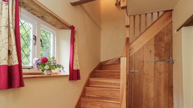 A wooden staircase with a handrail, a window with curtains, and a door with a metal handle. - Keepers Cottage (Devizes)