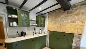 Une cuisine avec des meubles de couleur verte, un mur en pierre et un plan de travail blanc.