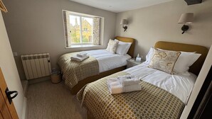 Une chambre d’hôtel avec deux lits, un radiateur, une fenêtre avec des rideaux et une table de chevet avec une lampe.