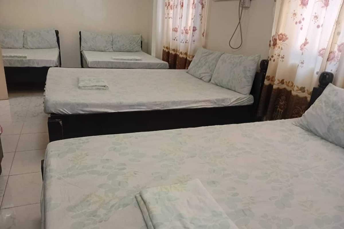 A hotel room with three single beds, a small table, and a chair.
