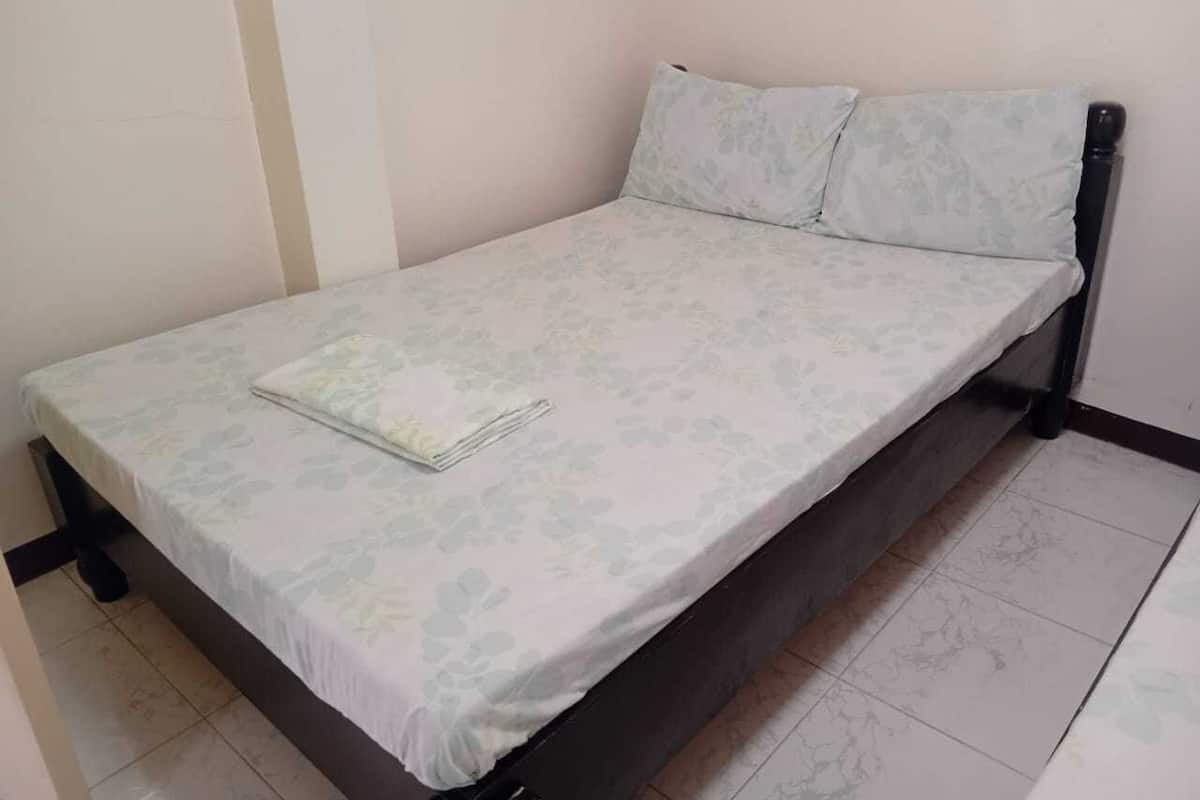 A single bed with a floral-patterned bedspread and two pillows, a black metal frame, and a white wall.