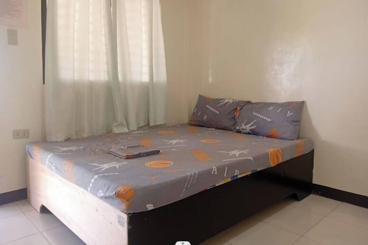 A single bed with a mattress cover featuring a pattern, a pillow, and a remote control on the bed.