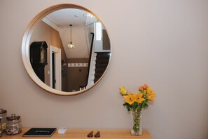 Un miroir rond accroché au mur, un vase rempli de fleurs jaunes et une table en bois sur laquelle se trouvent un livre et une paire de chaussures.