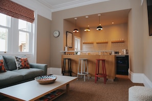 Una sala de estar acogedora con sofá, mesa de centro y una cocina americana con taburetes y encimera.