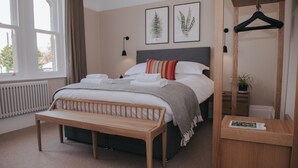 Ein ordentlich eingerichtetes Schlafzimmer mit einem Bett, einer Bank, einem Nachttisch, einer Pendelleuchte und einem Fenster.