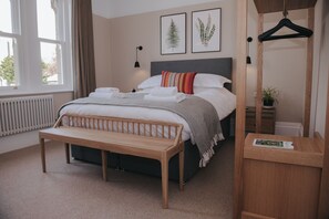 A neatly arranged bedroom with a bed, a bench, a bedside table, a hanging light, and a window.