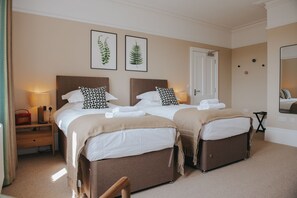 Quarto de hotel com duas camas, mesa de cabeceira de madeira, espelho e gravuras botânicas emolduradas na parede.