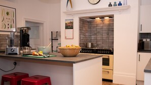 Eine moderne Küche mit einer zentralen Kochinsel, roten Barhocker, einer Kaffeemaschine, einem Mixer und einer Uhr an der Wand.