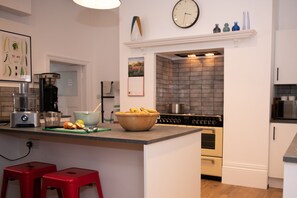 Una cocina moderna con una isla central, taburetes rojos, una cafetera, una licuadora y un reloj en la pared.