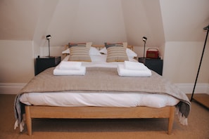 Una cama bien hecha con una manta y almohadas estampadas, dos mesitas de noche con lámparas, y una radio roja sobre una de ellas.