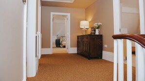 Un couloir doté d’un revêtement de sol en moquette, une armoire en bois avec une lampe, et une porte donnant sur une autre pièce.
