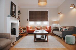 Una sala de estar con chimenea, dos sofás, una mesa de centro y un ventanal con persianas.